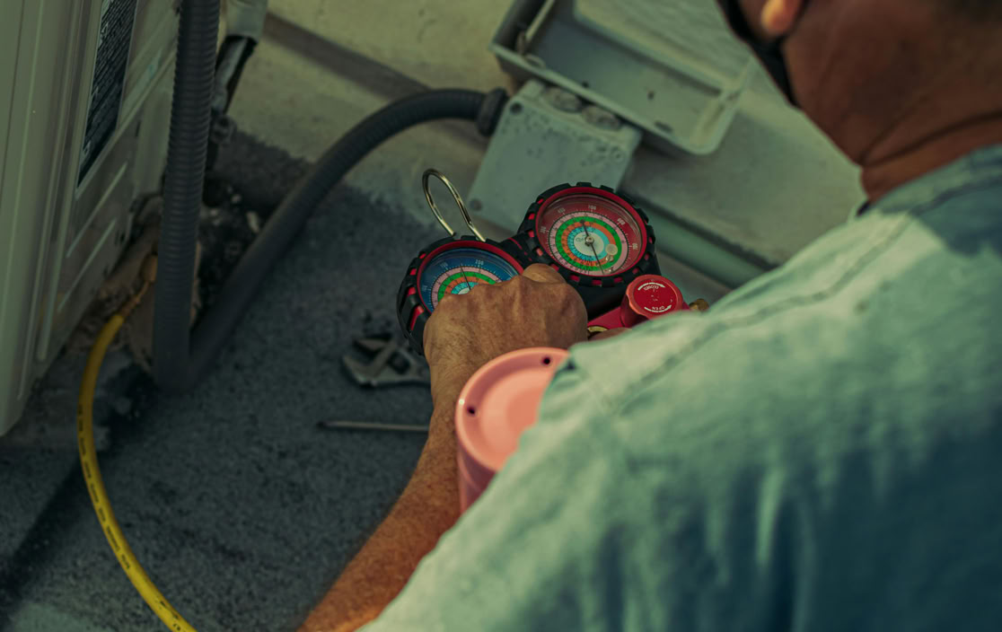 Professional technician repairing an outdoor air conditioning unit with gauges and tools.